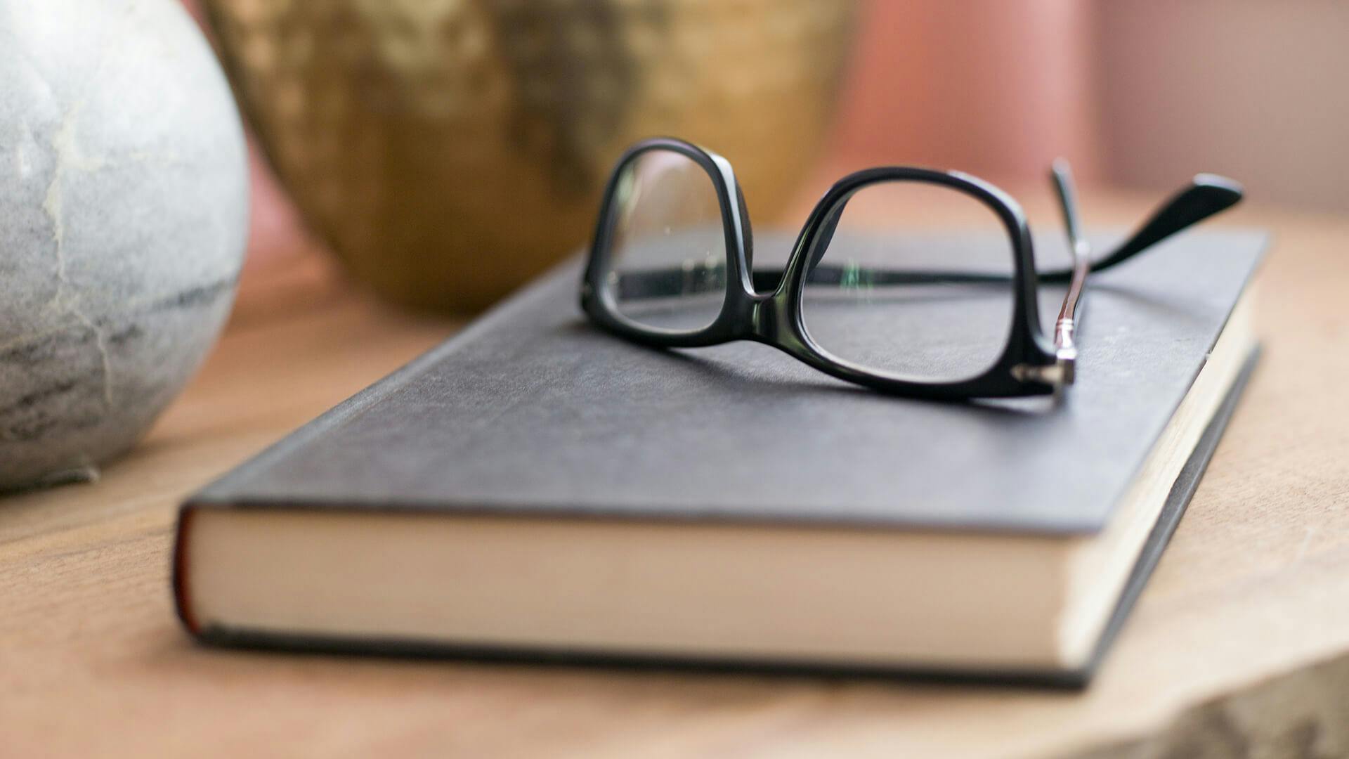 Glasses sitting on a book with a vase in the background