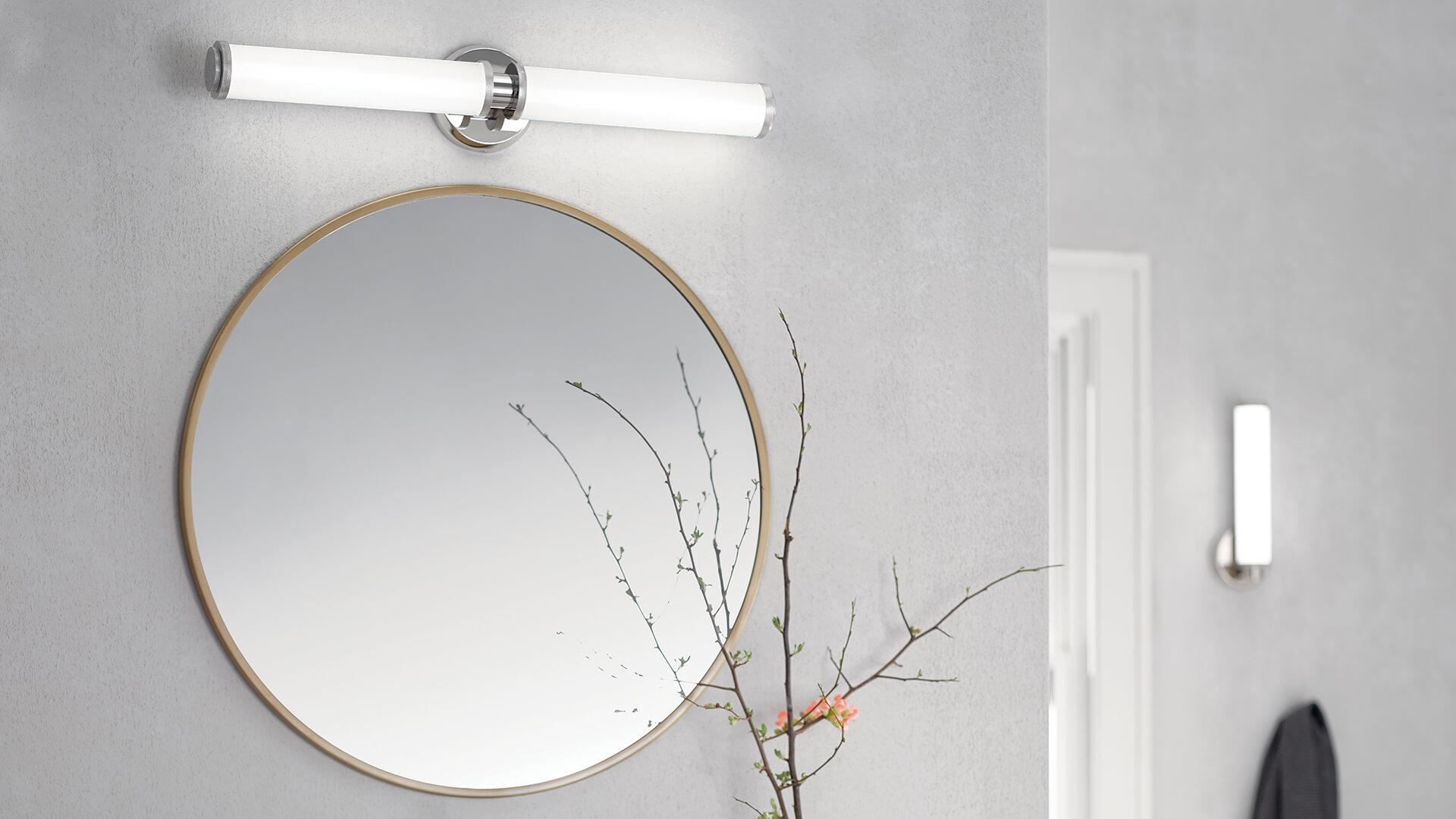 White bathroom wall featuring a mirror with a Indeco vanity light above it and a wall sconce in the background