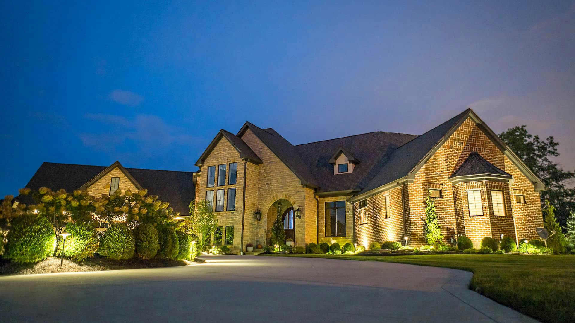 View of exterior of home from driveway at dusk, exterior lighting is on.