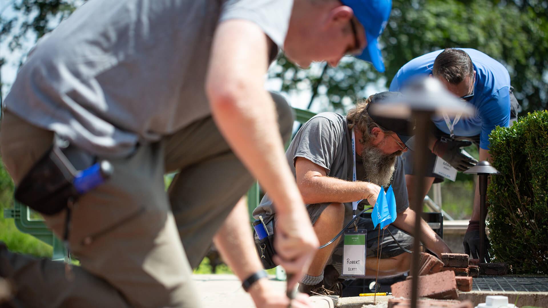 Three men working together to install in ground lights on a walking path during the day.