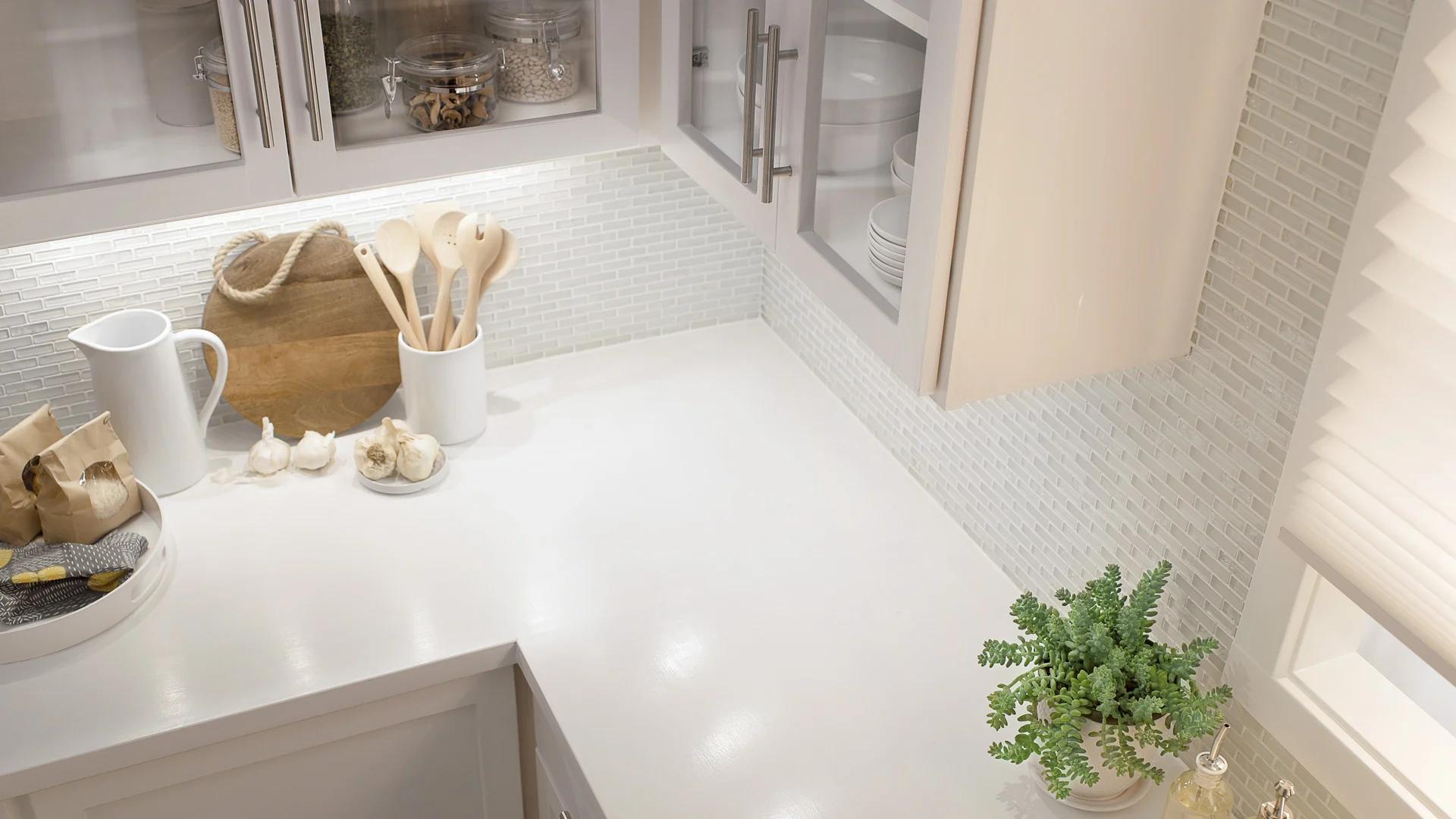 Over head angle of a kitchen counter with white cabinets and countertop being lit by under cabinet lights.