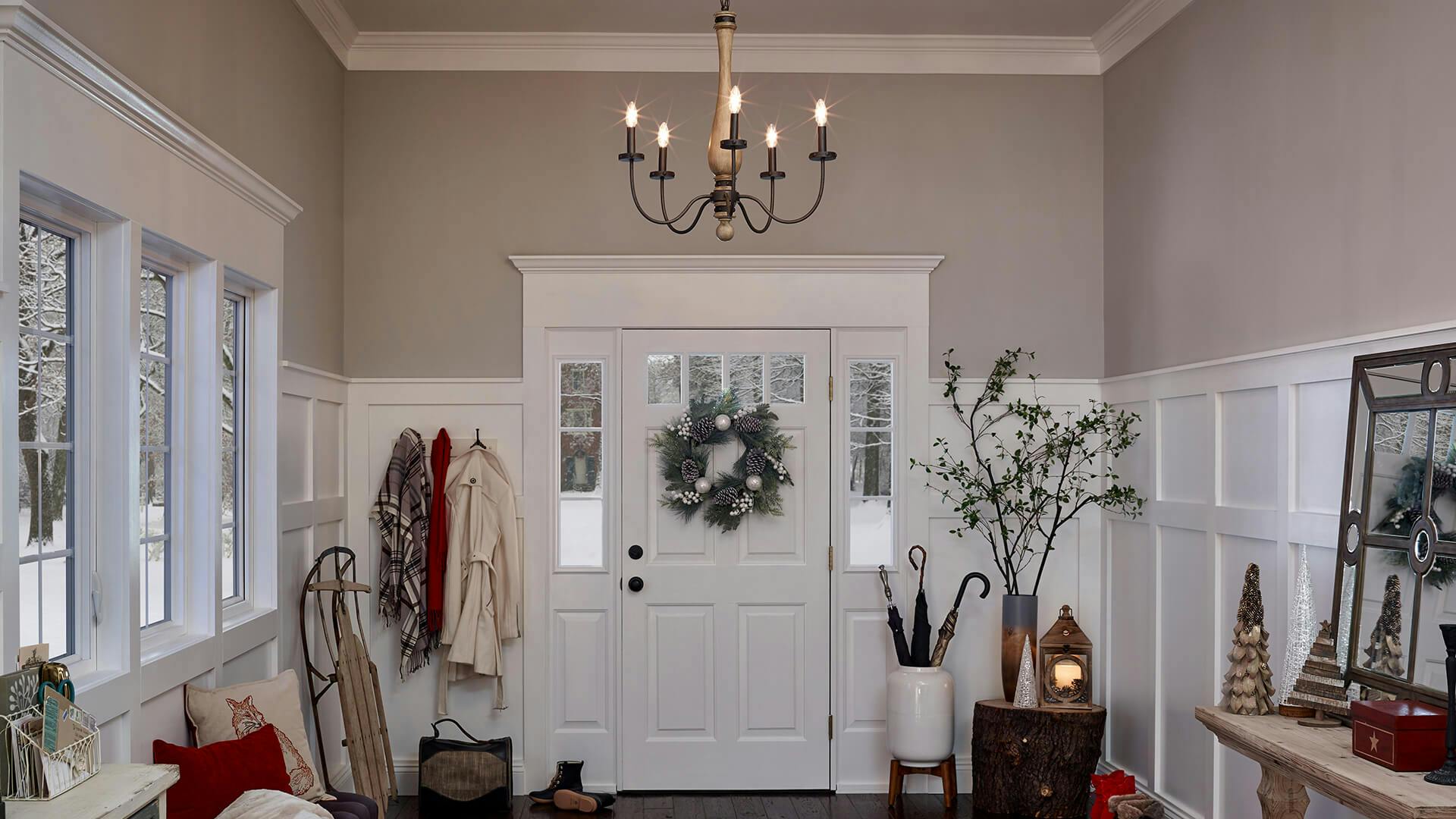 Evan chandelier hanging in the center of a foyer decorated with various holiday and winter items