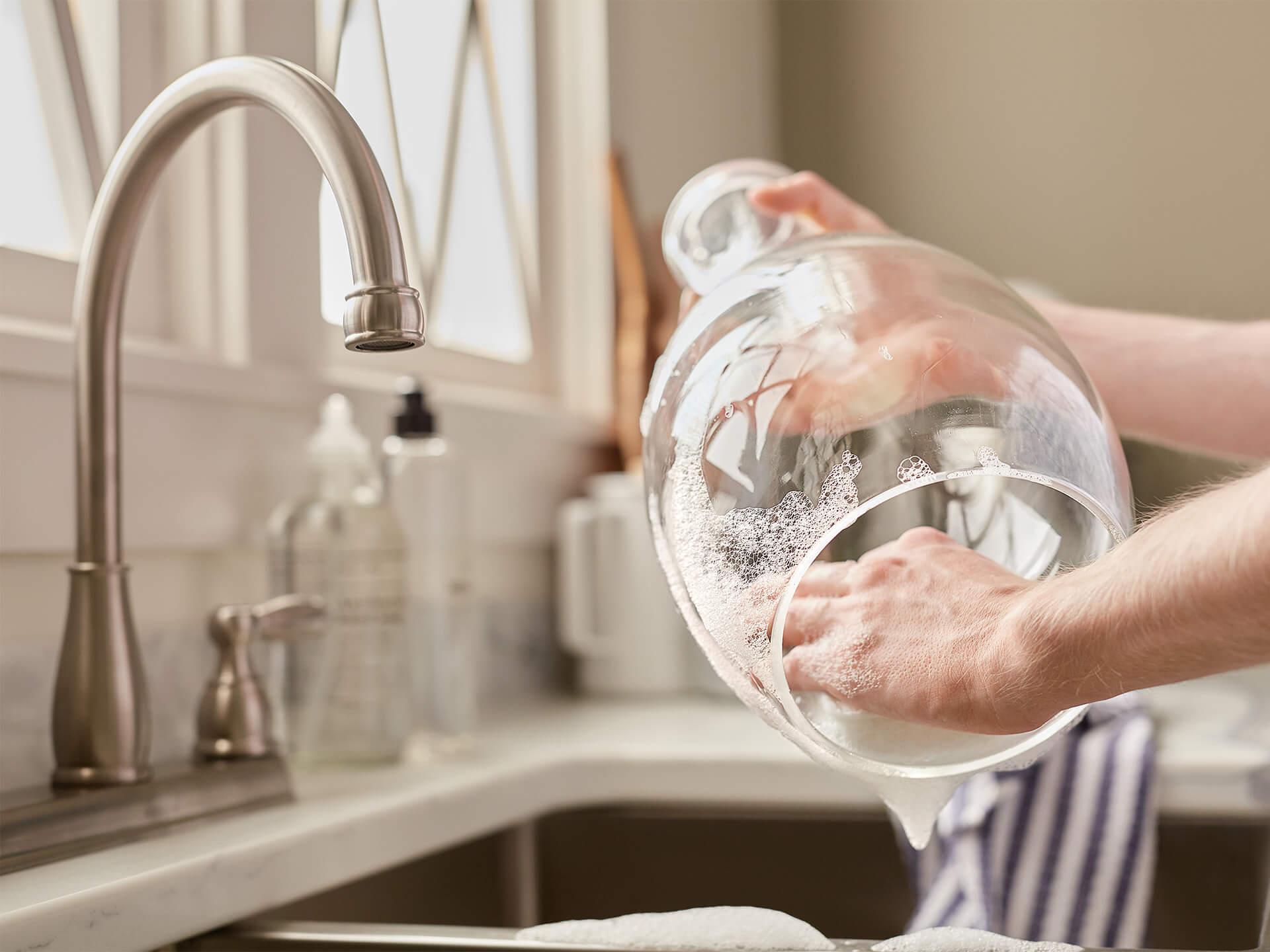 A glass shade of a sconce being hand washed with a sponge over a kitchen sink