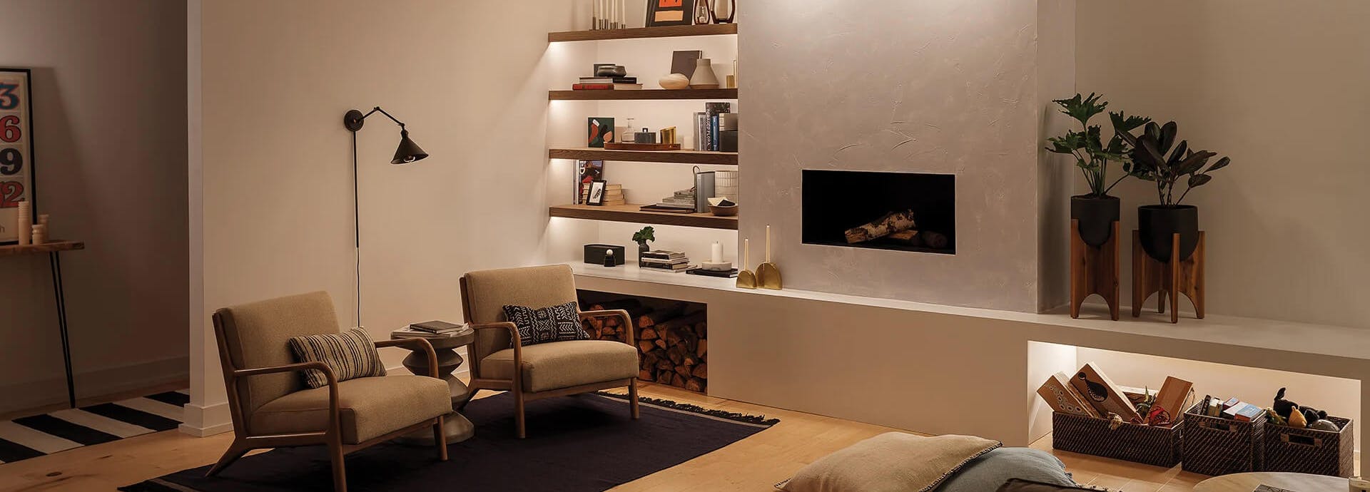 Reading nook at daytime illuminated by three ceiling lights above the fireplace, channel lighting on a mounted bookshelf and an Ellerbeck sconce above two nearby chairs