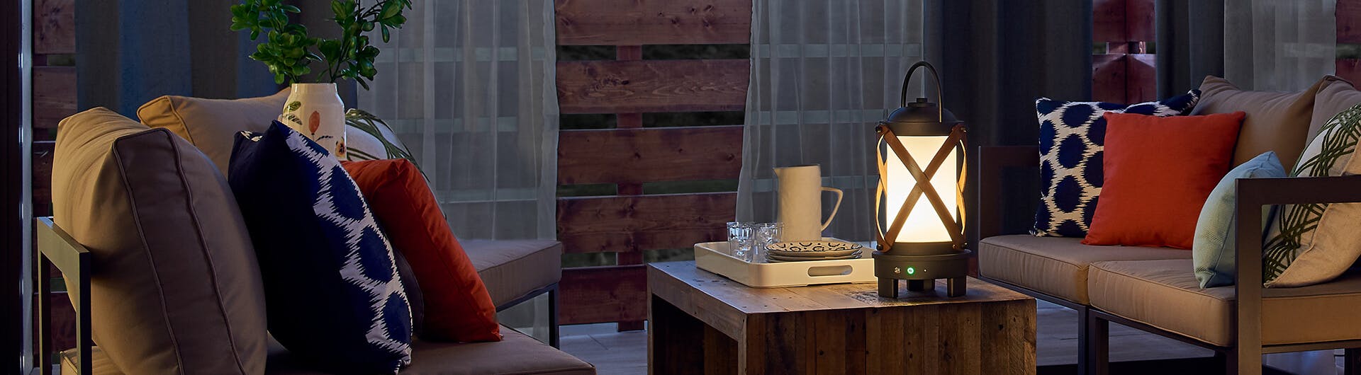 Patio at night with a lantern on a coffee table with couches on either side.