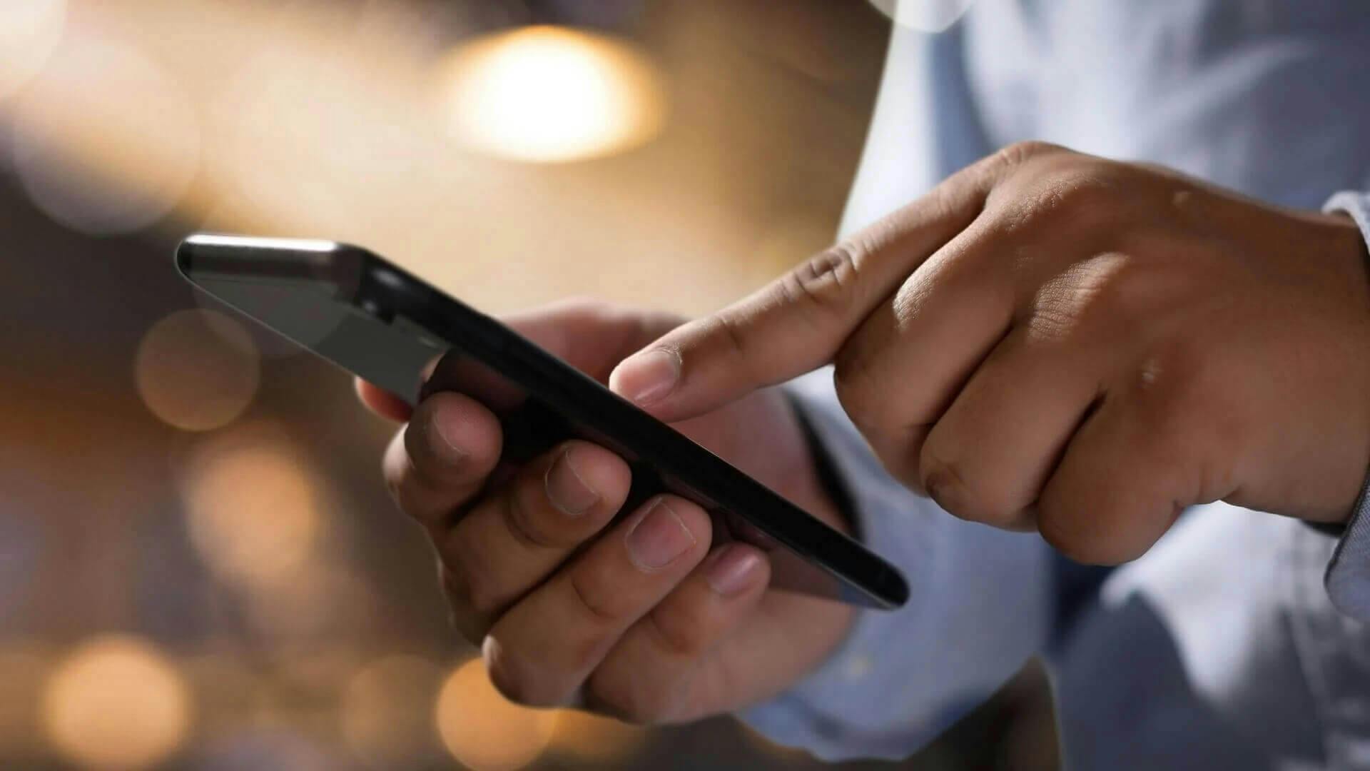 Close up of a man's hands holding a phone with blurred lights in the background