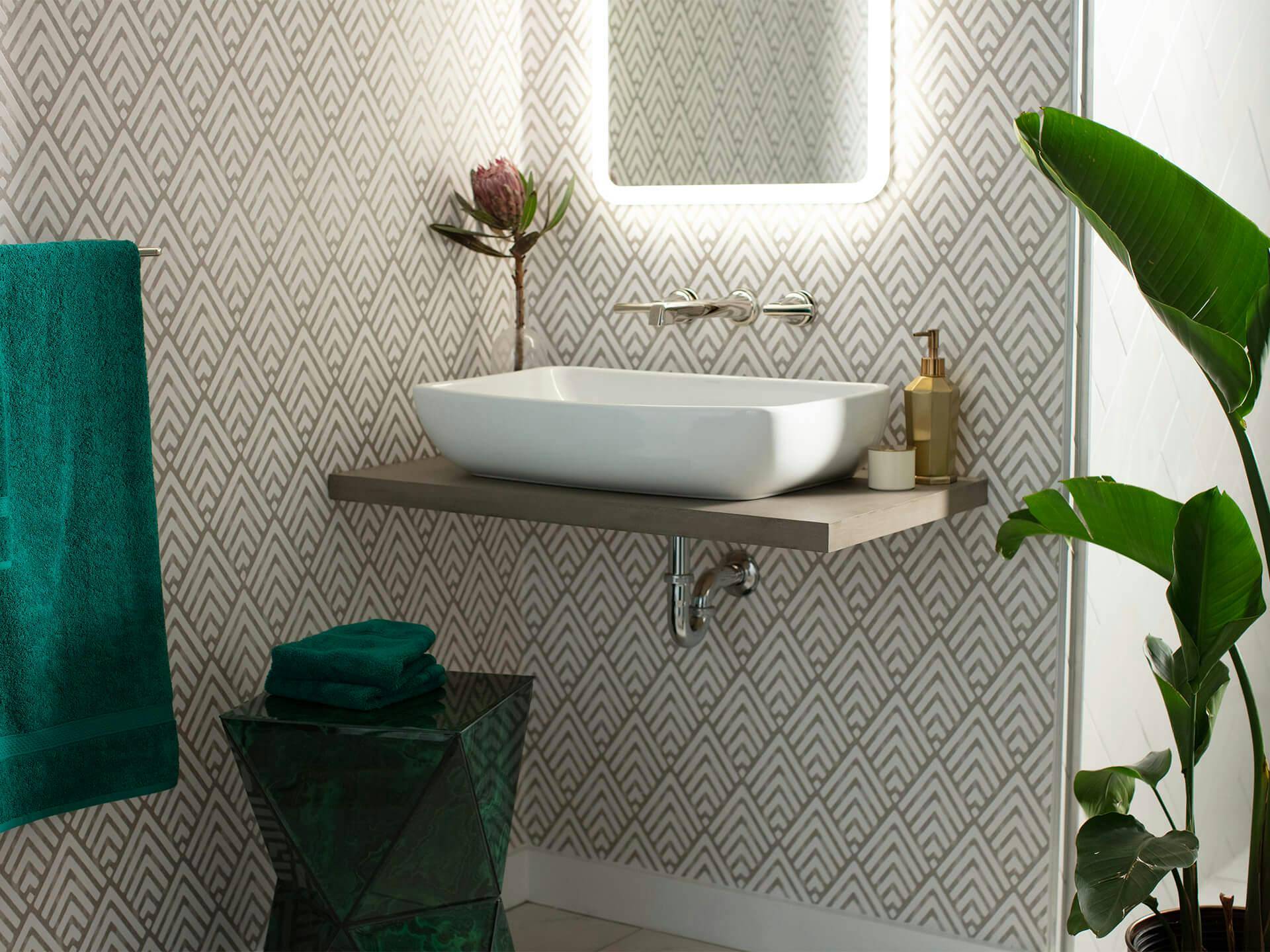 Bathroom sink surrounded by green towels, a standing plant