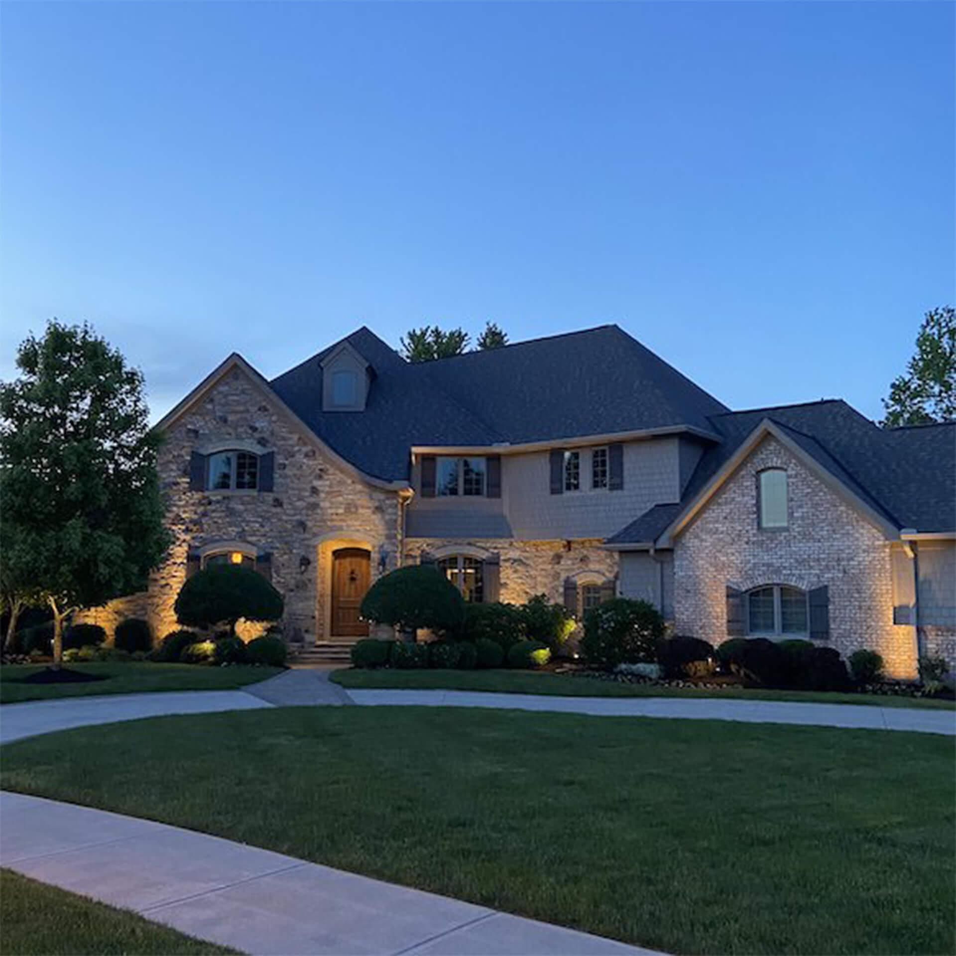 View of exterior of home from driveway at dusk, exterior lighting is on.