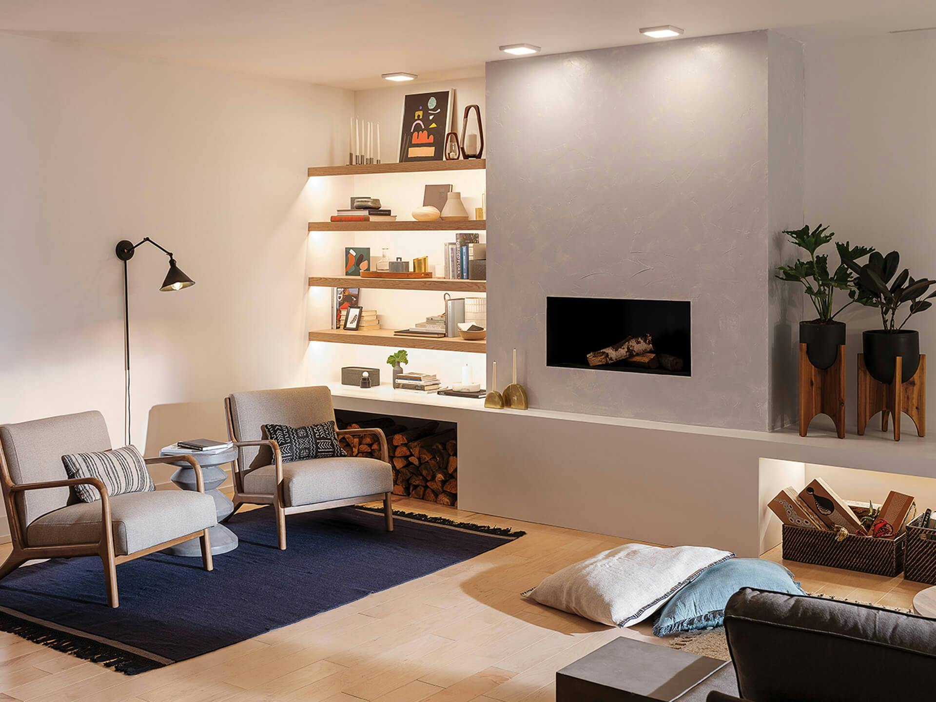 Reading nook at daytime illuminated by three ceiling lights above the fireplace, channel lighting on a mounted bookshelf and an Ellerbeck sconce above two nearby chairs