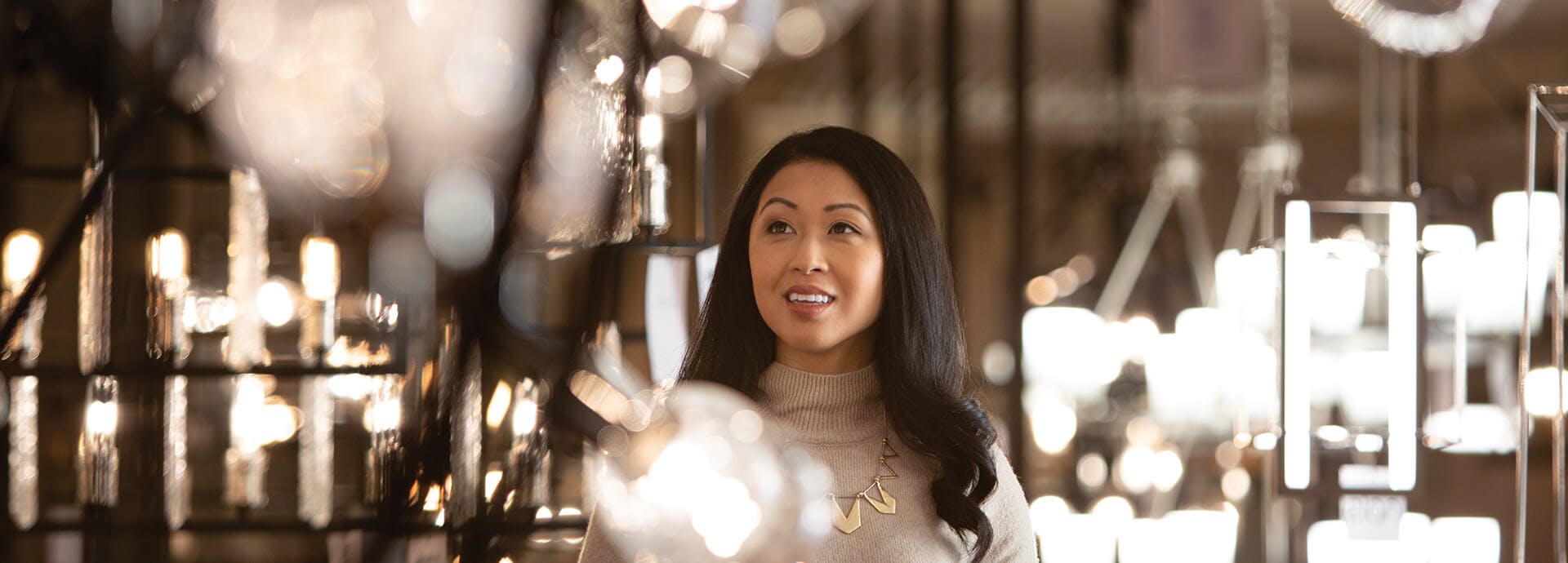 Woman smiling while looking upwards towards a variety of chandeliers that are hanging at her height