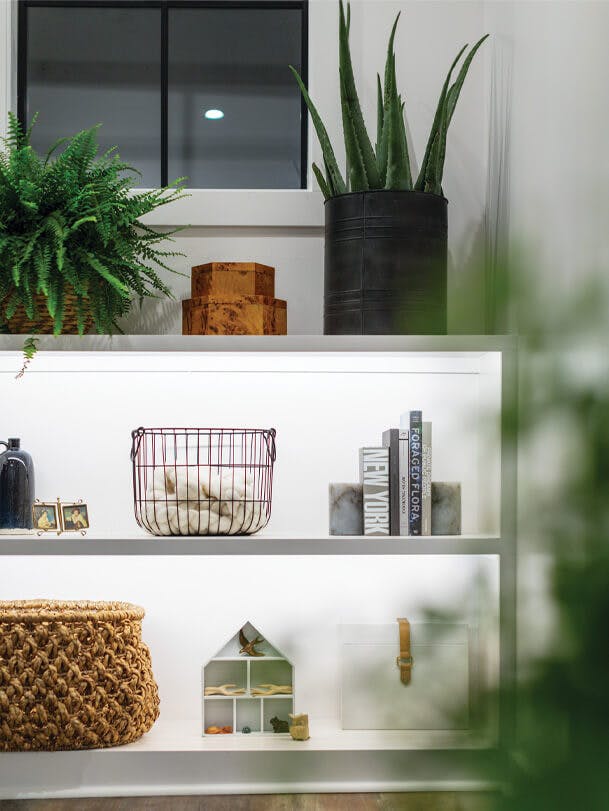 White shelf with variety of knick-knacks such as a basket, plants, books, and doll house