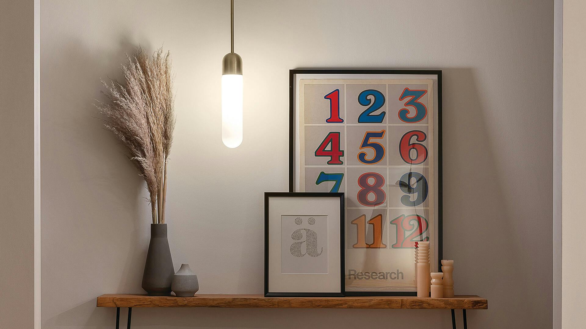 Table in a hallway housing a decorative plant, candles and a couple photos with a glowing Sorno pendant hanging above