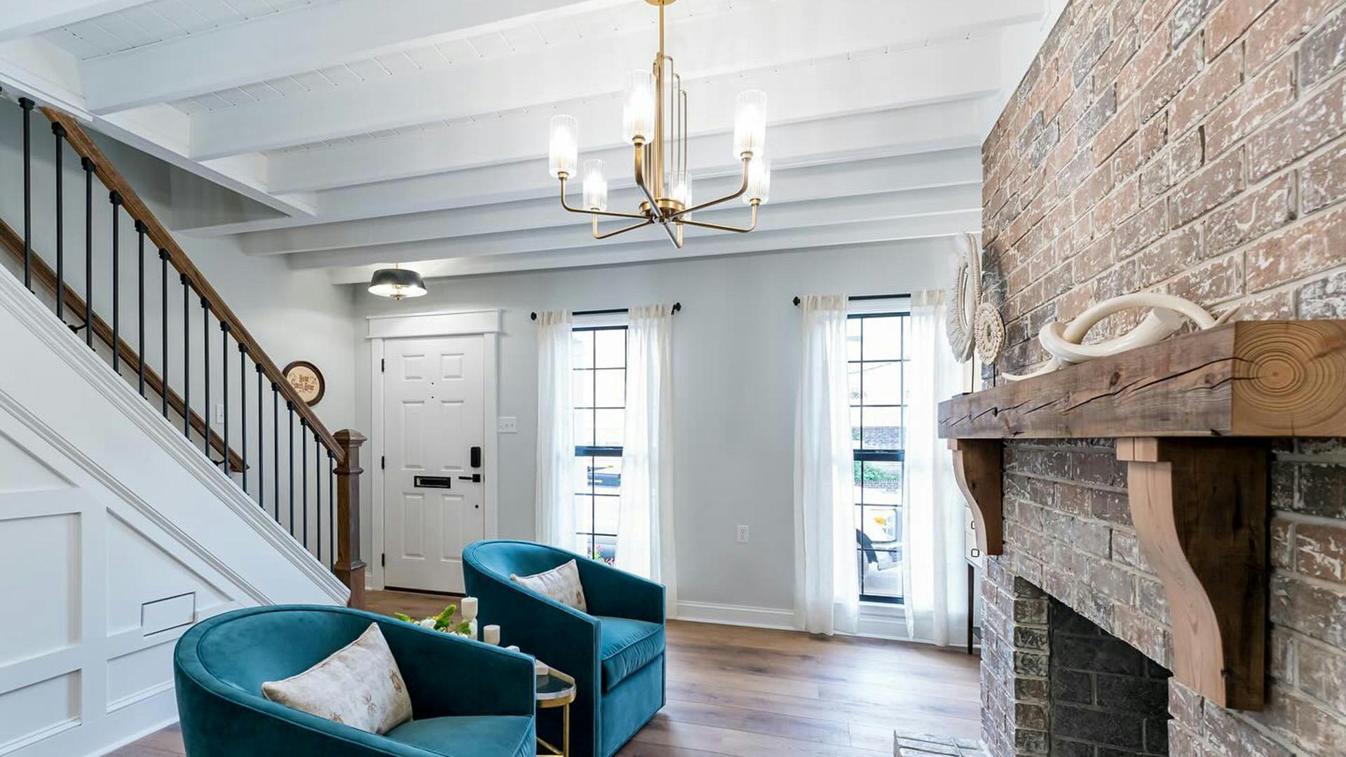 Interior living room with 2 blue chairs featuring a large brick fireplace and Kimrose chandelier 