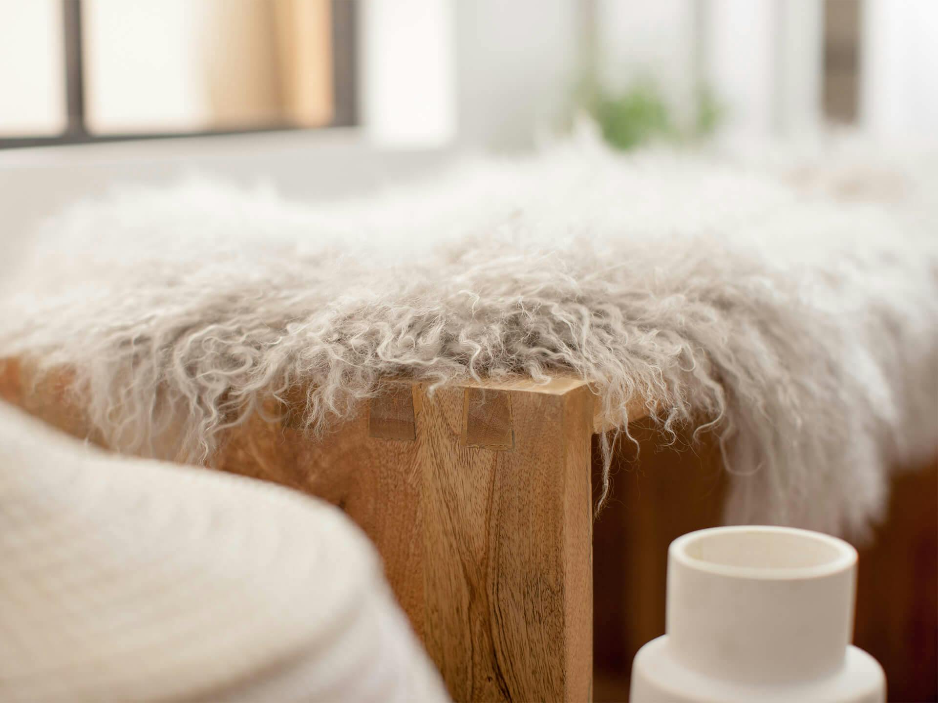 Lifestyle imager of a bench with a white fuzzy blanket draped over it 