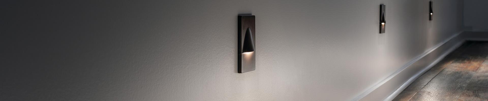 Three lit wall-mounted LED step lights leading down a hallway