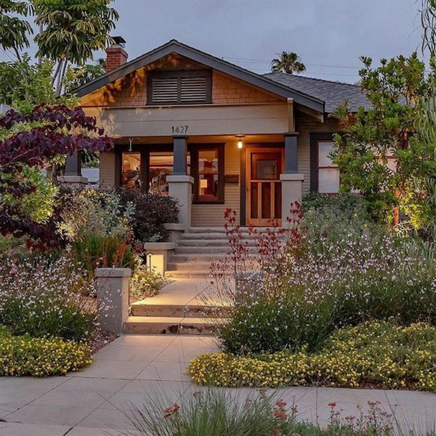 Exterior image of the front of a house with wood finishes with a front porch light turned on giving a warm glow on the patio in the evening