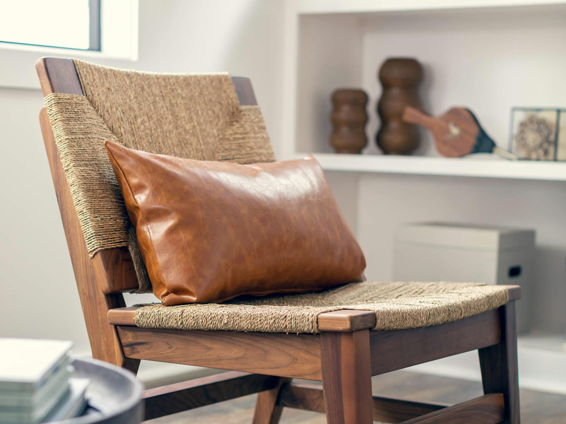 Close up of a wood and rattan chair with a brown leather throw pillow