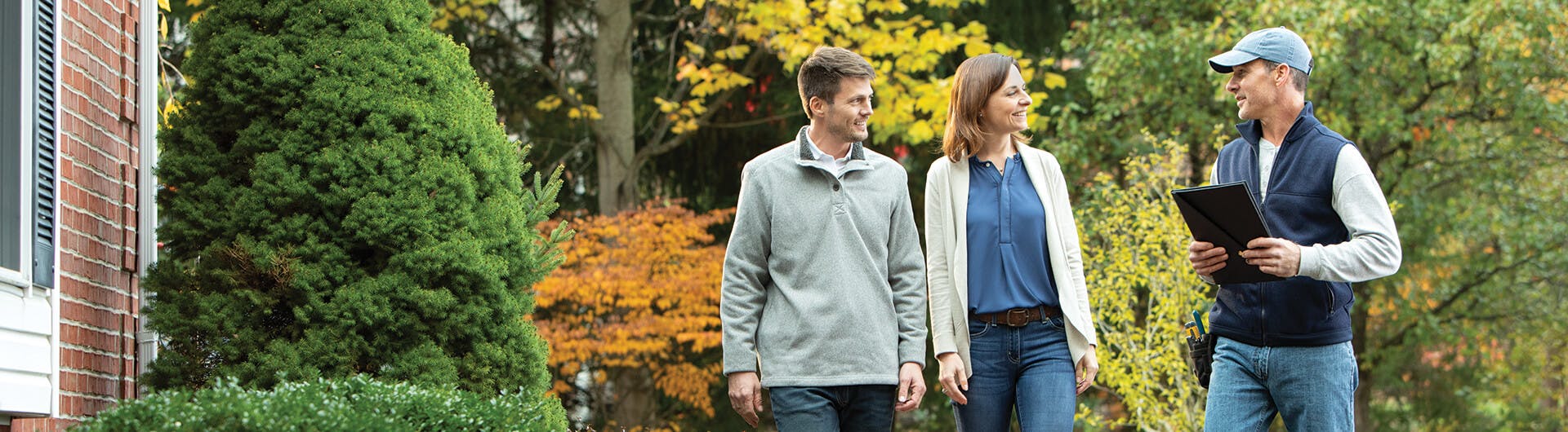 Man and woman walking with a man holding a clipboard outside a home