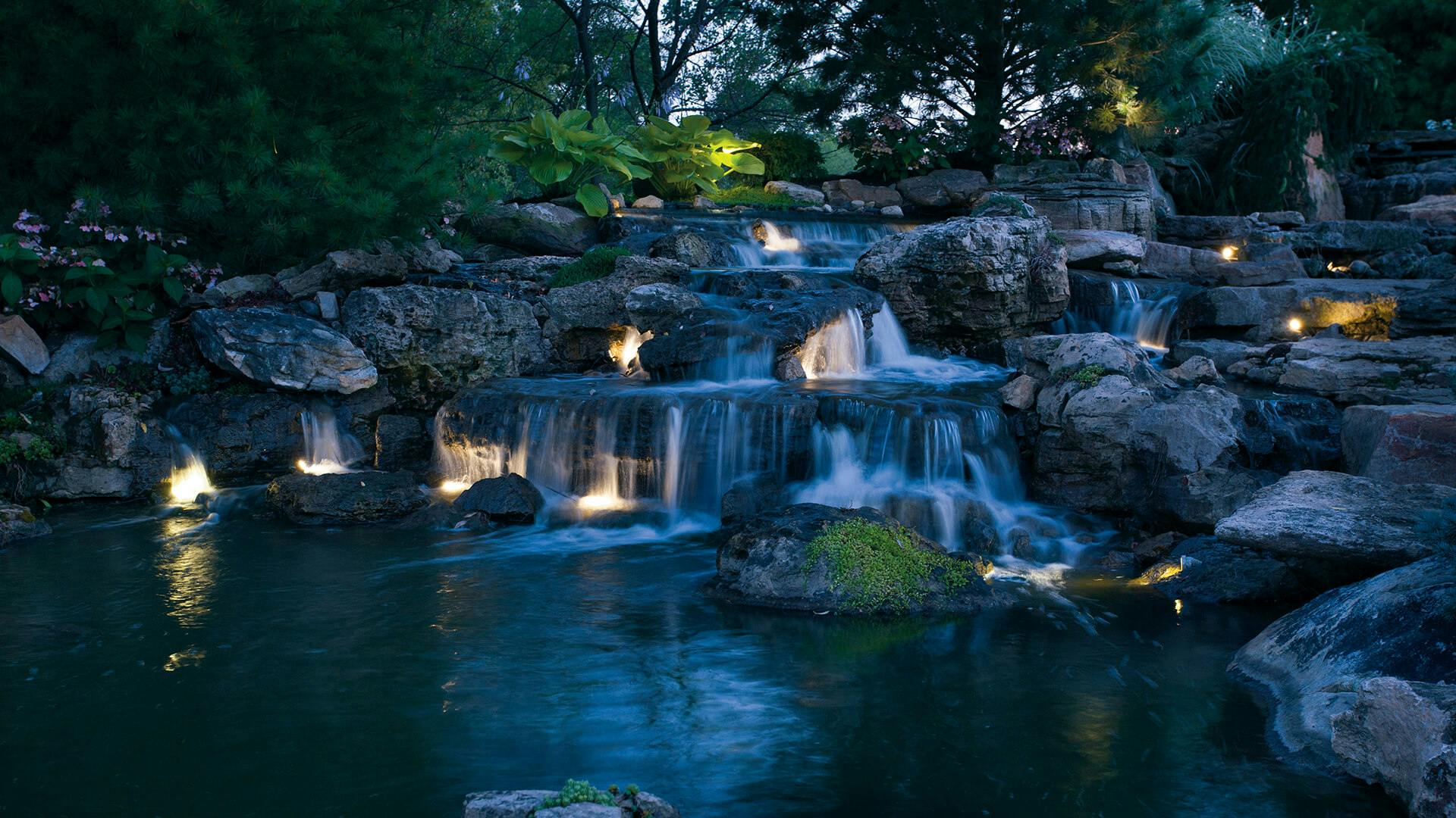 Large waterfall with variety of levels and small up and down lighting sprinkled throughout behind the flowing water.