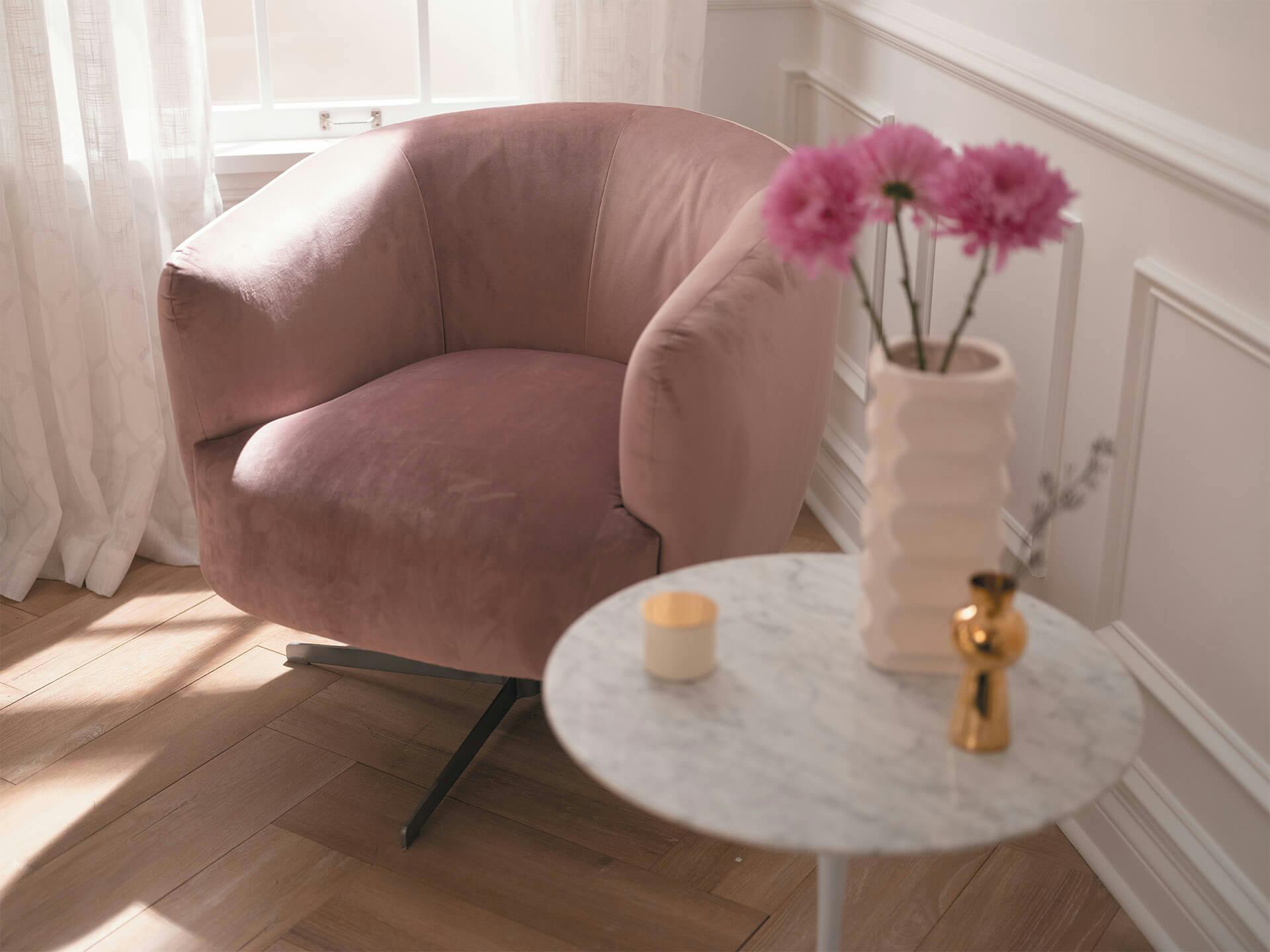 Sitting area in living room with rose pink char and flowers in vase.