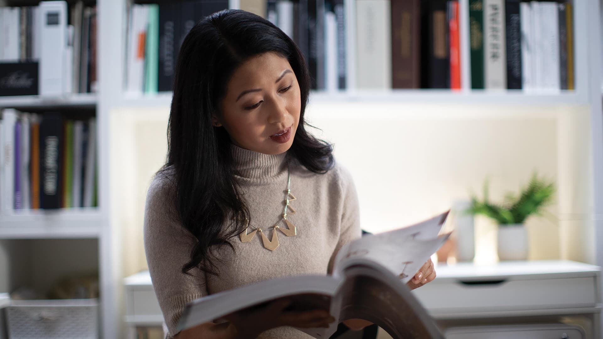 Interior designer flipping through a book with a library of books behind her