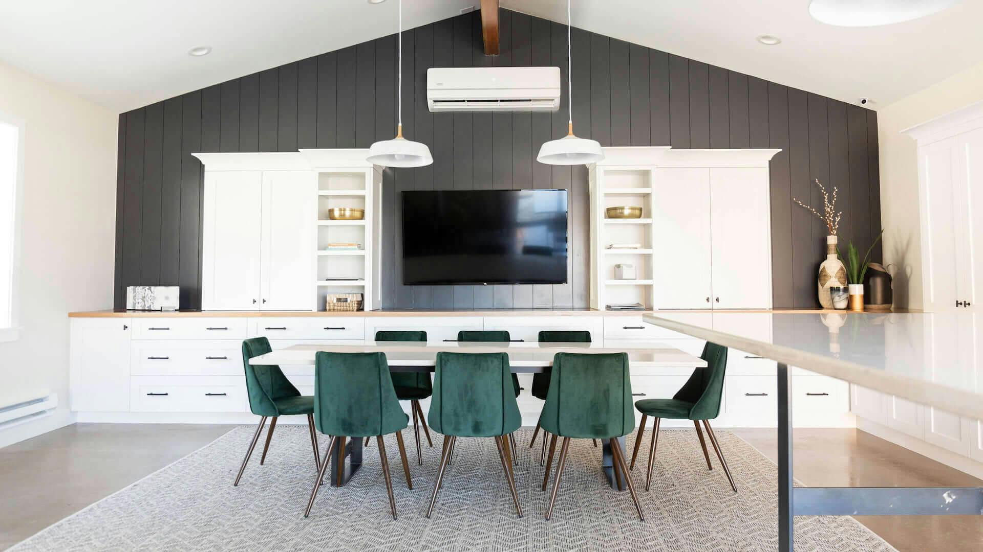 Modern dining room with tall ceilings and green velvet chairs at a long white table.