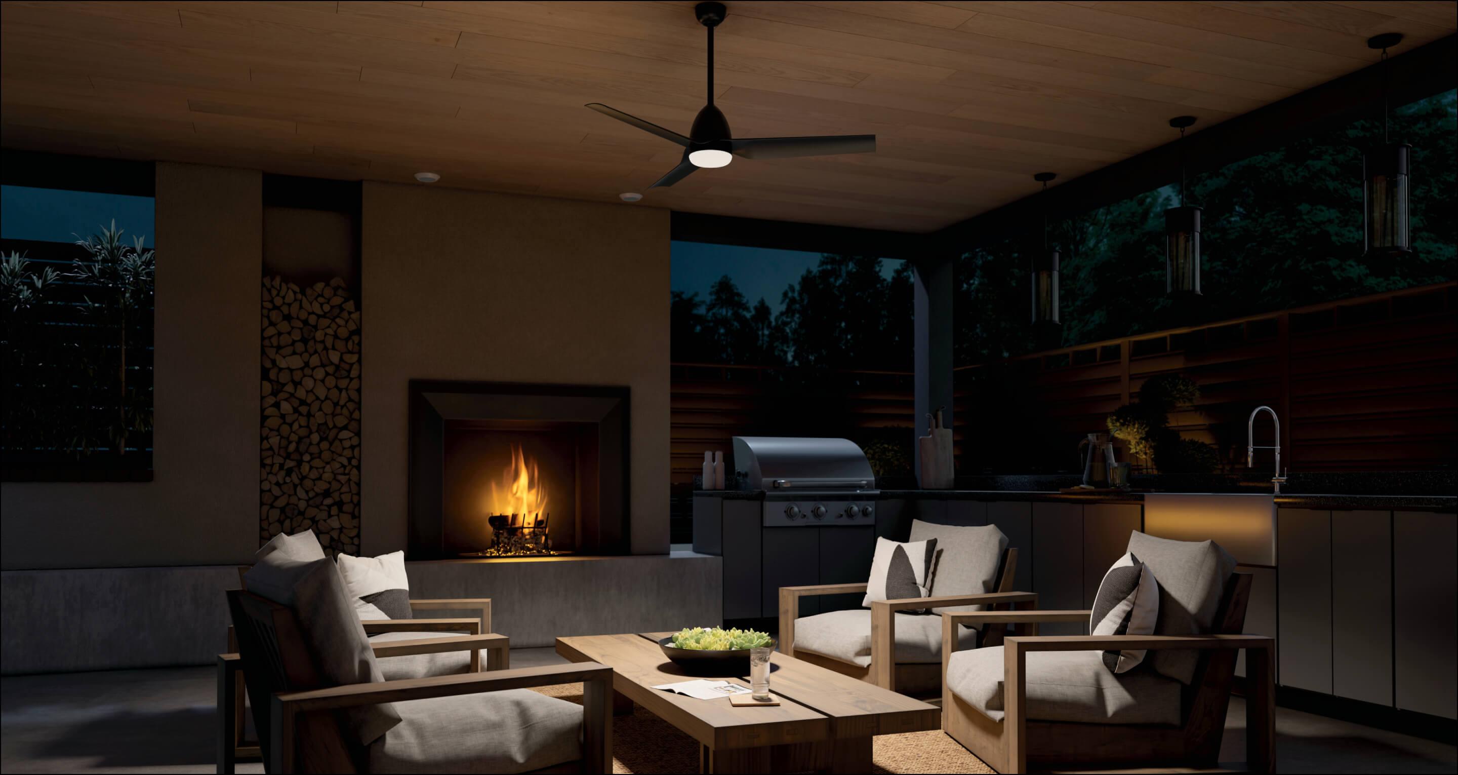 Outdoor kitchen at night lit only by a Fit ceiling fan in the center of the room and the fireplace